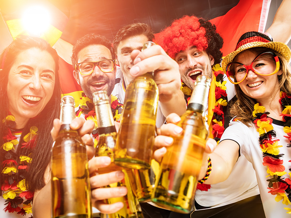 Mehrere Fußball-Fans feiern gemeinsam und stoßen mit Flaschen an. Sie tragen Fan-Artikel in den deutschen Nationalfarben